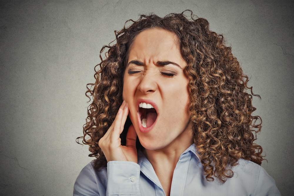 Closeup portrait young woman with sensitive tooth ache crown problem about to cry from pain touching outside mouth with hand isolated grey wall background. Negative emotion facial expression feeling